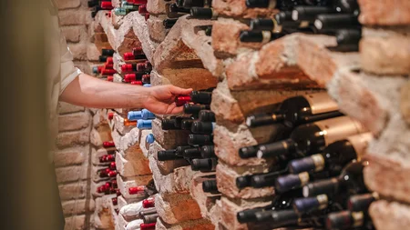 Hand nimmt Weinflasche aus einem Backstein-Weinregal