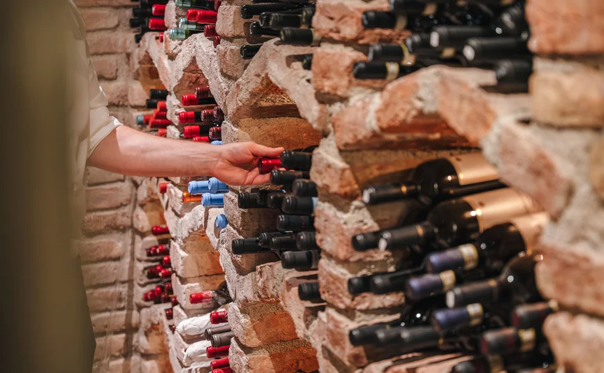 Hand nimmt Weinflasche aus einem Backstein-Weinregal