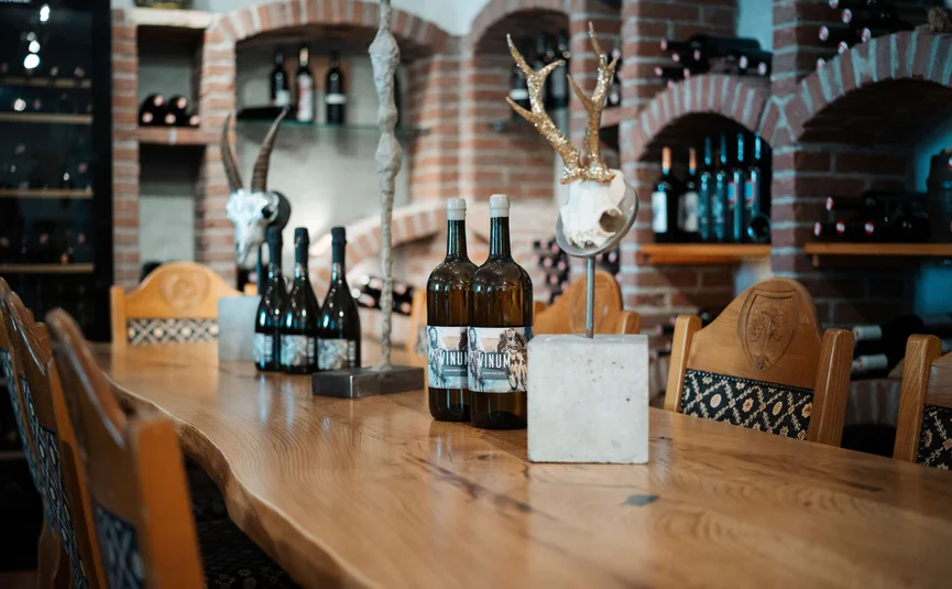 Weinkeller mit Holzbank, Weinflaschen und dekorativen Schädeln an der Tischmitte