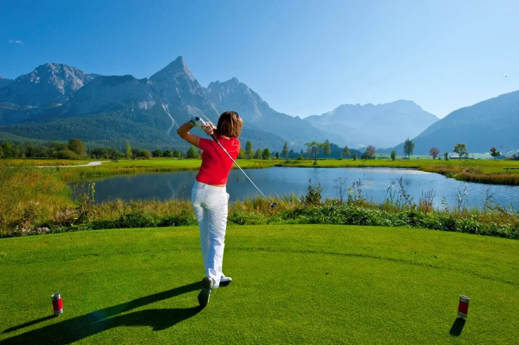 Frau spielt Golf vor Berglandschaft und See bei klarem Himmel