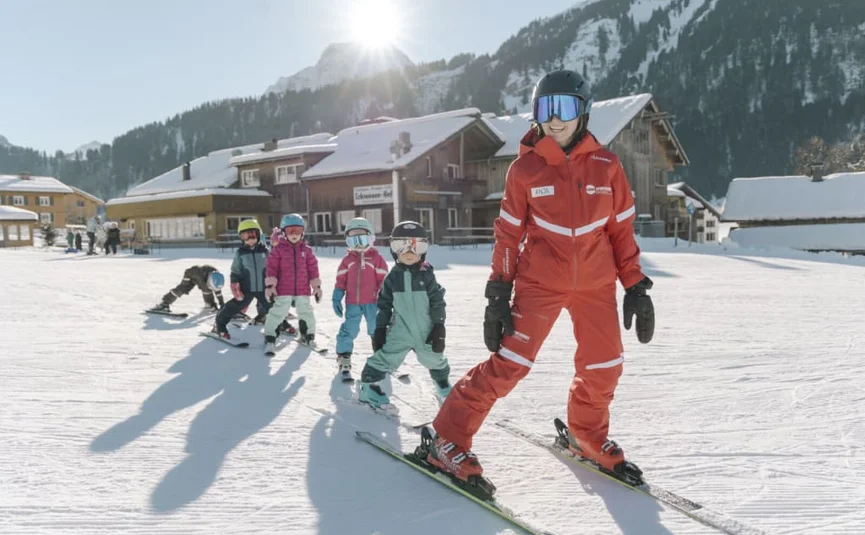 Ski instructor leading children in a beginner class on snow with mountains behind