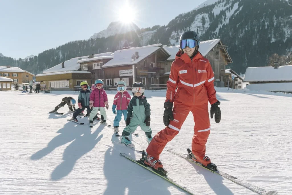 Skilehrerin führt Kinder bei einem Anfängerkurs im Schnee mit Bergen im Hintergrund