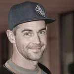 Mann mit schwarzer Baseballkappe lächelt in Innenraum