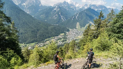 Two mountain bikers on forest trail overlooking valley and mountains