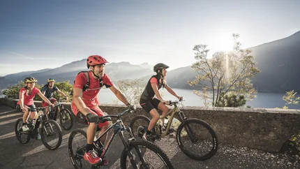 Group of cyclists riding mountain bikes on road with lake view at sunset