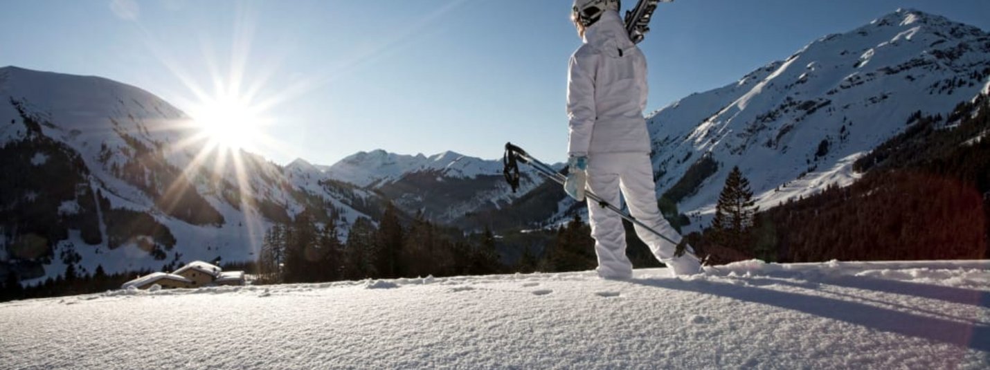 Schönruh Holiday Special 6=7 + Top Snow Card Skier carrying person looks at sunny snowy mountains