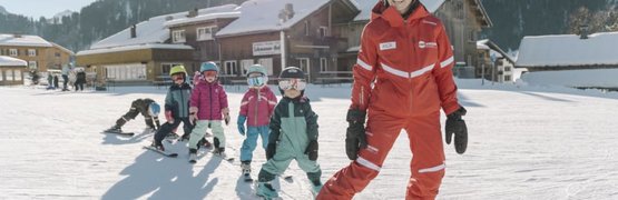 Skilehrerin führt Kinder in bunten Skibekleidungen auf schneebedecktem Hang