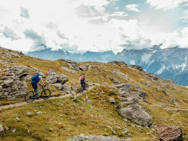 Twee mountainbikers op een rotsachtig bergpad onder bewolkte lucht