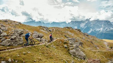 Twee mountainbikers op een rotsachtig bergpad onder bewolkte lucht