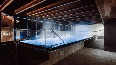 Bike & Wellness Heated outdoor pool with wooden roof structure and steam at night