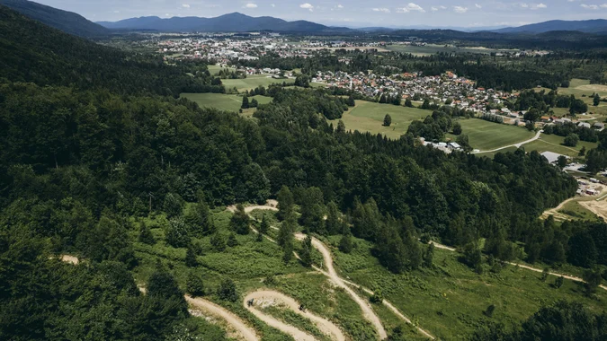 Mountain Bike Holidays © Klemen Humar - MTBTrailCenter Luftaufnahme eines Waldgebietes mit Wanderwegen und Stadt in der Ferne