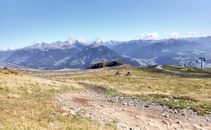 Fahrradfahrer auf Bergweg mit Alpen im Hintergrund und Sessellift