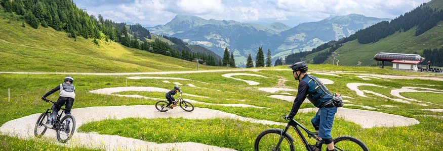 Drei Mountainbiker fahren auf einem kurvigen Weg in den Bergen bei bewölktem Himmel