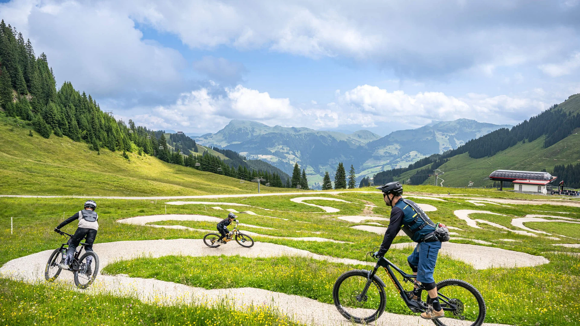 Drei Mountainbiker fahren auf einem kurvigen Weg in den Bergen bei bewölktem Himmel