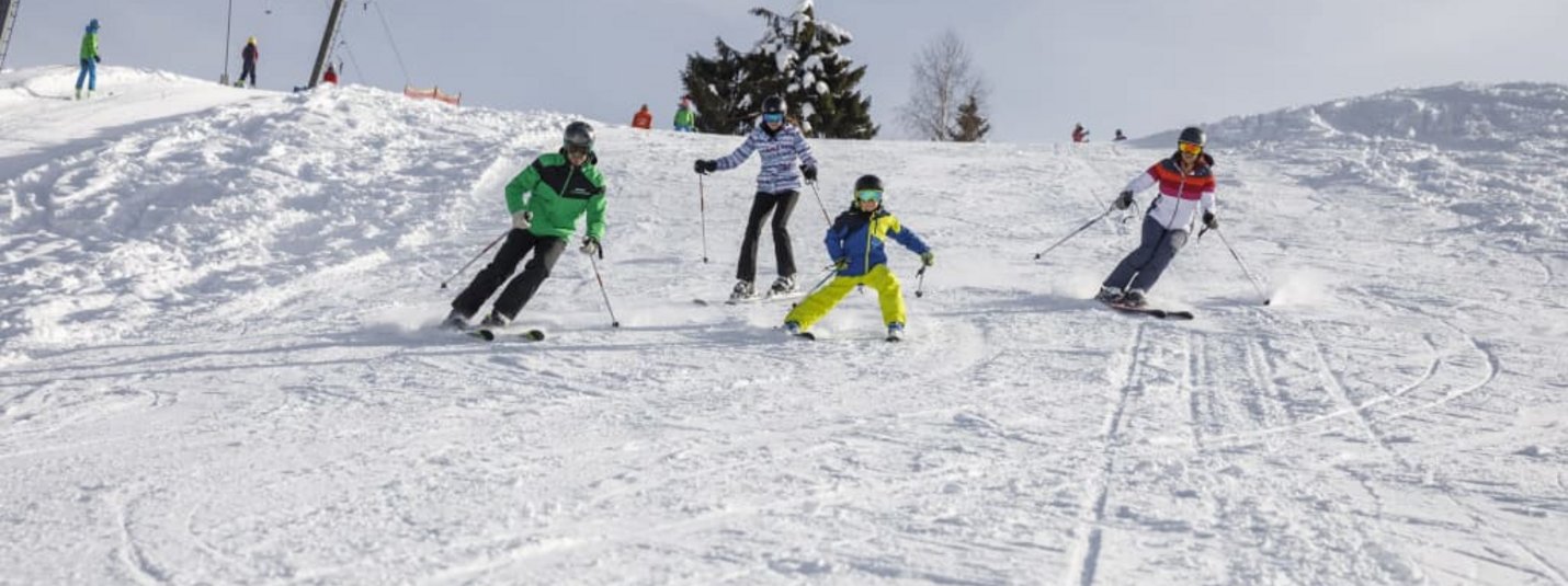 Vier Skifahrer fahren auf schneebedeckter Piste bei bewölktem Himmel