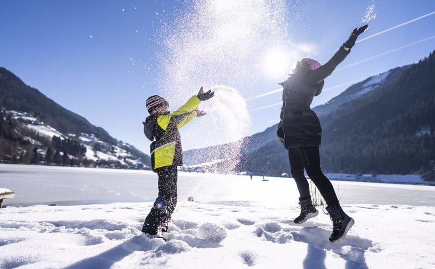 Two people playing in the snow with mountains in the background on a sunny day