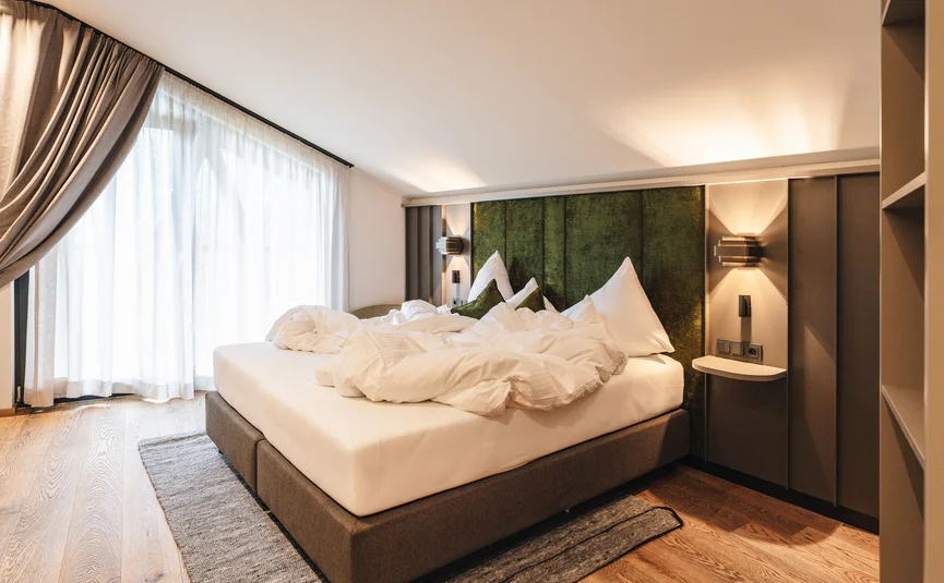 Unordentliches Bett in modernem Schlafzimmer mit grünem Kopfteil und Holzboden