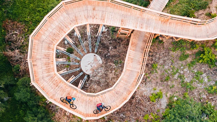 Die besten Touren & Trails der Alpen © Patrick Wasshuber Radfahrer auf spiralförmiger Holzbrücke in grünem Wald