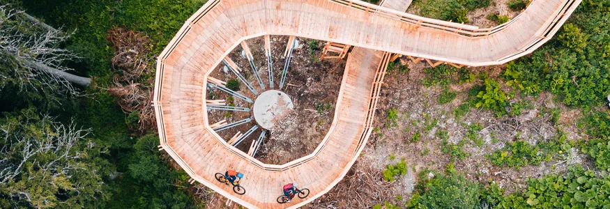 Ein perfekter Enduro-Tag – vom ersten Höhenmeter bis zum letzten Trail © Patrick Wasshuber Radfahrer auf spiralförmiger Holzbrücke in grünem Wald