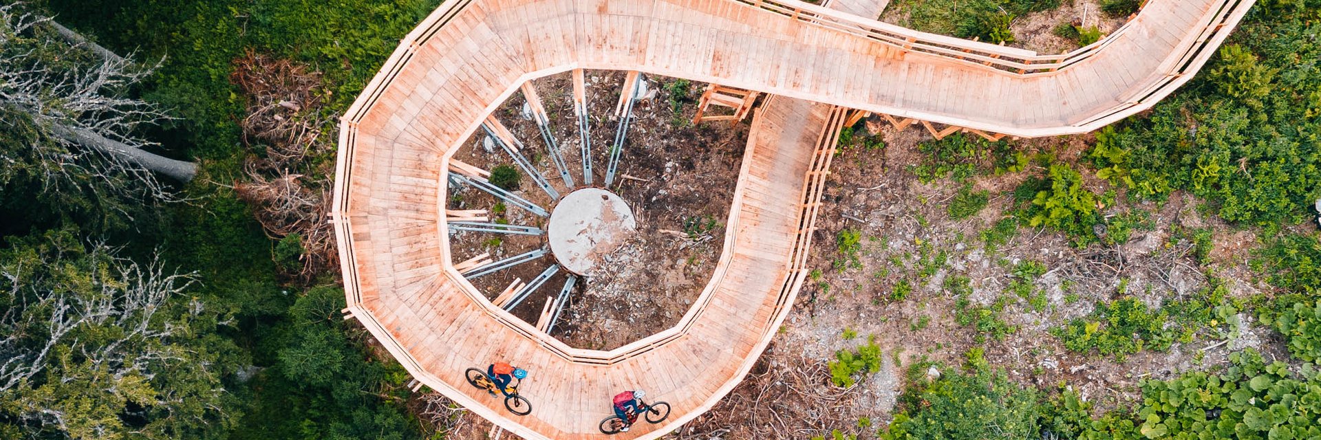 Radfahrer auf spiralförmiger Holzbrücke in grünem Wald