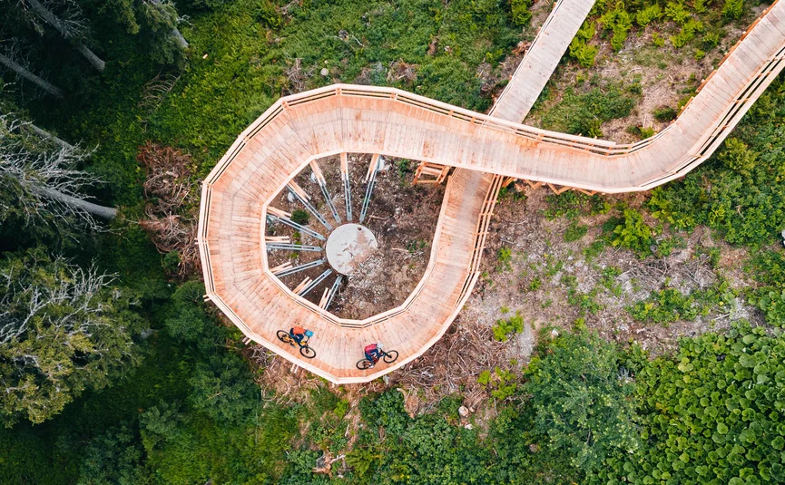Radfahrer auf spiralförmiger Holzbrücke in grünem Wald