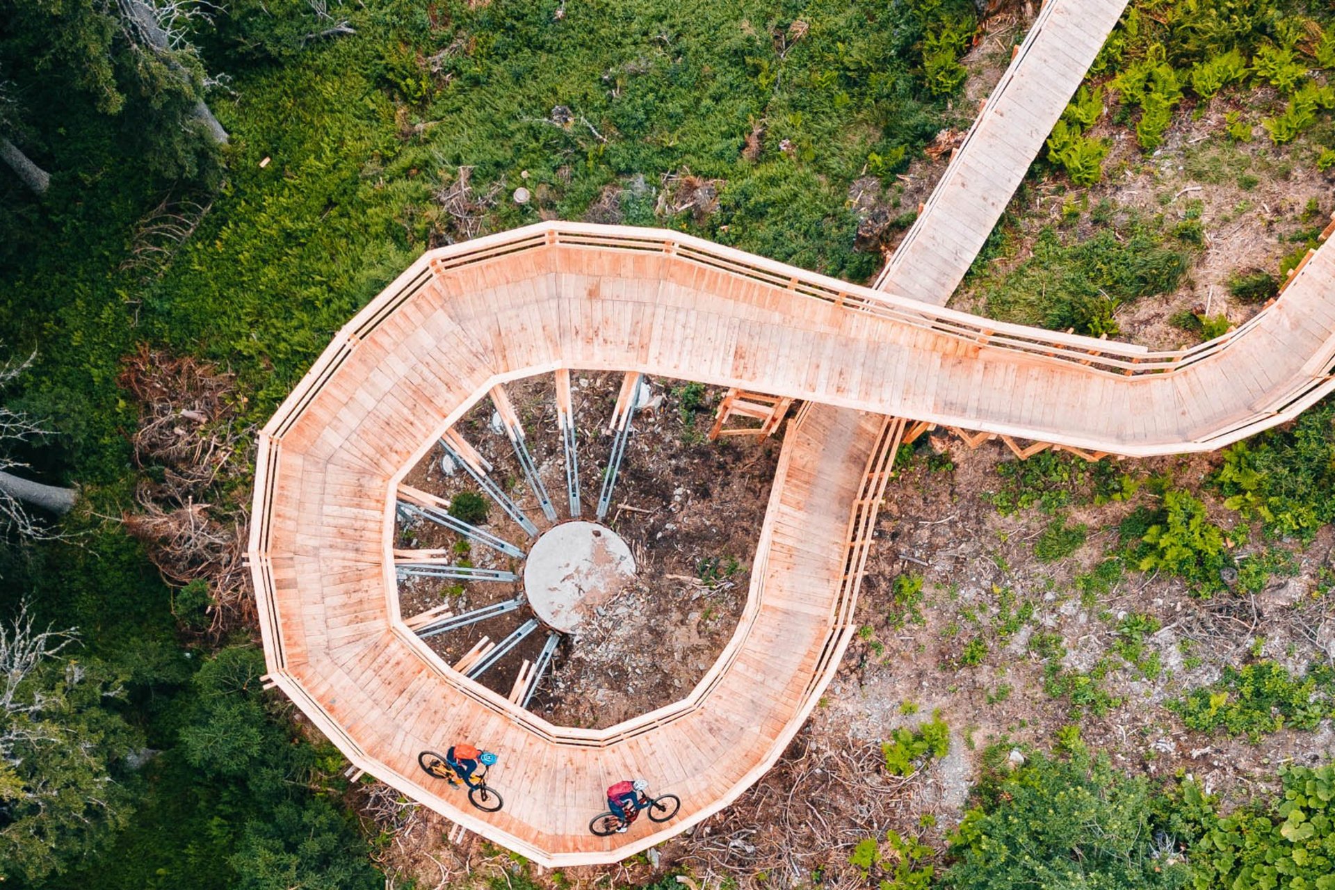 Radfahrer auf spiralförmiger Holzbrücke in grünem Wald