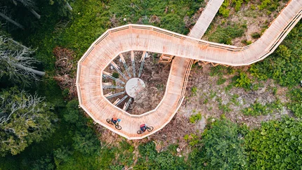 Radfahrer auf spiralförmiger Holzbrücke in grünem Wald