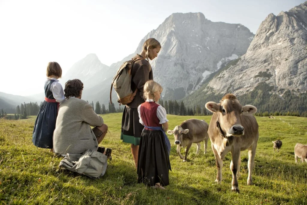 Familie beobachtet Kühe auf einer Wiese vor Bergkulisse