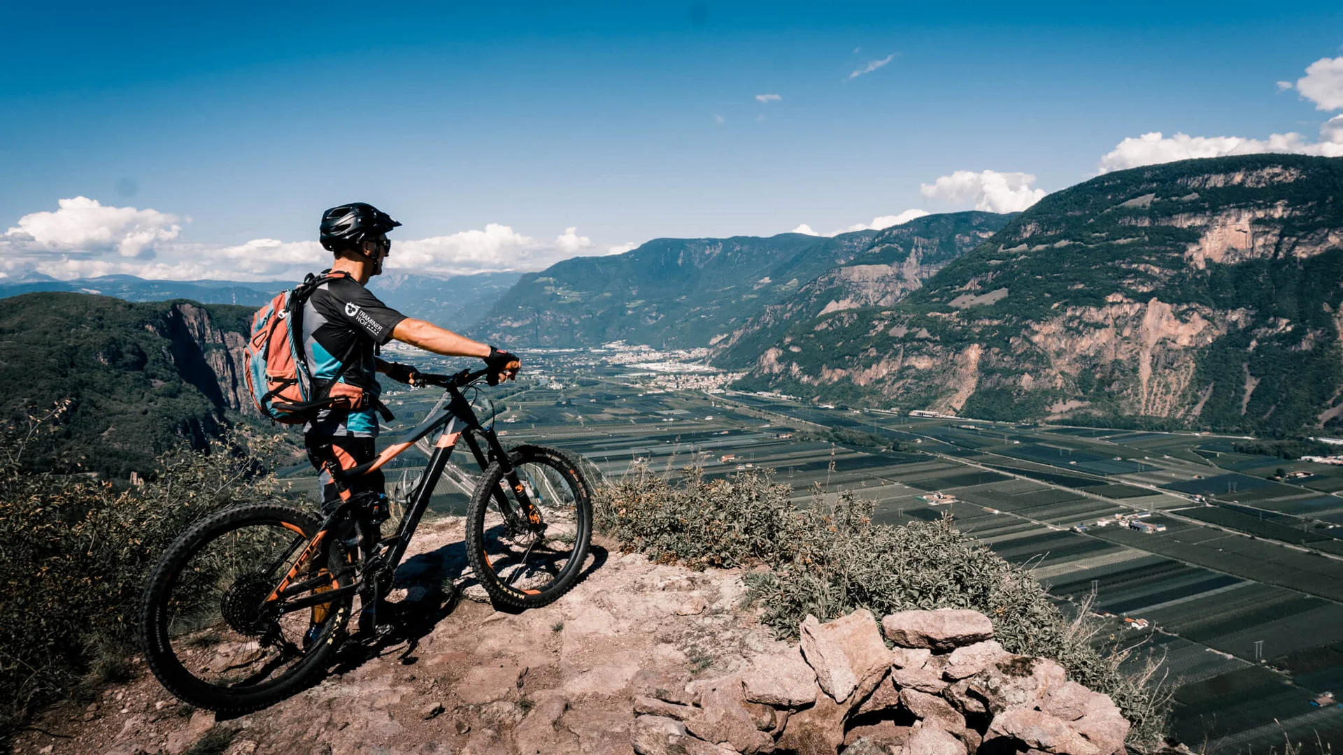 Mountainbiker blickt von Berg auf Tal mit Feldern und Bergen