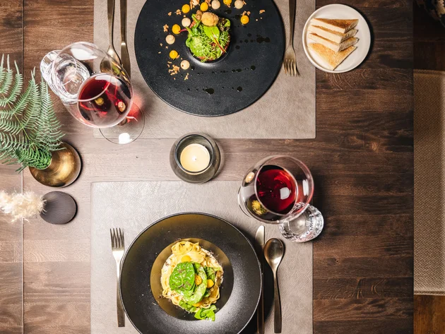 Elegantes Abendessen mit Wein, Pasta und Salat auf dunklem Holztisch