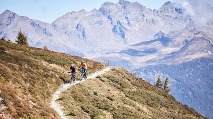 Zwei Radfahrer auf Bergweg mit Alpen im Hintergrund