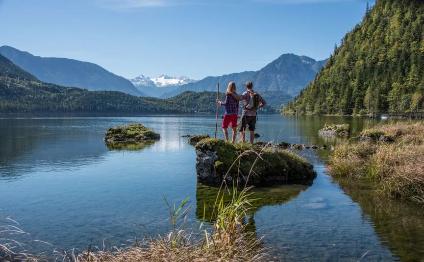Couple standing by lake shore with mountain landscape and clear sky