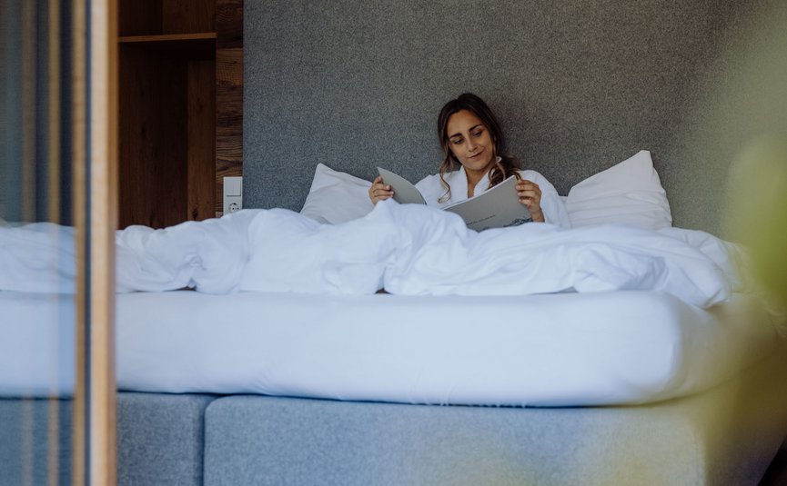 Puradies © creatingclick Frau liest entspannt ein Buch im Bett mit Holzverkleidung im Hintergrund