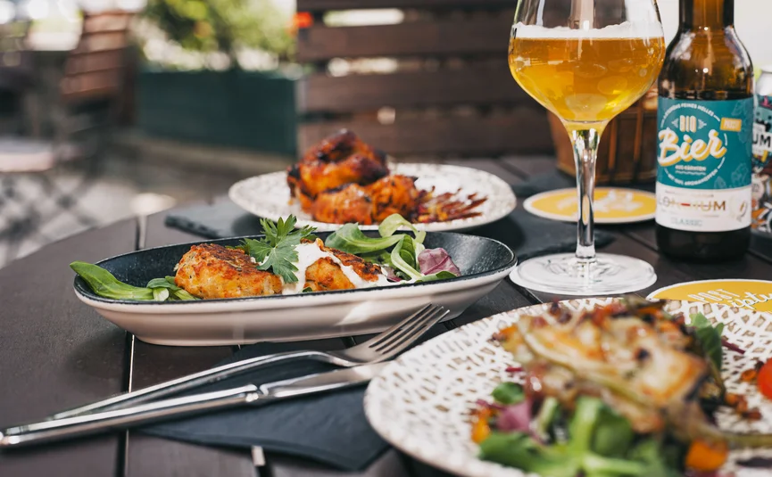Tisch mit Bierglas, Bierflasche und Tellern mit Hähnchengerichten und Salat