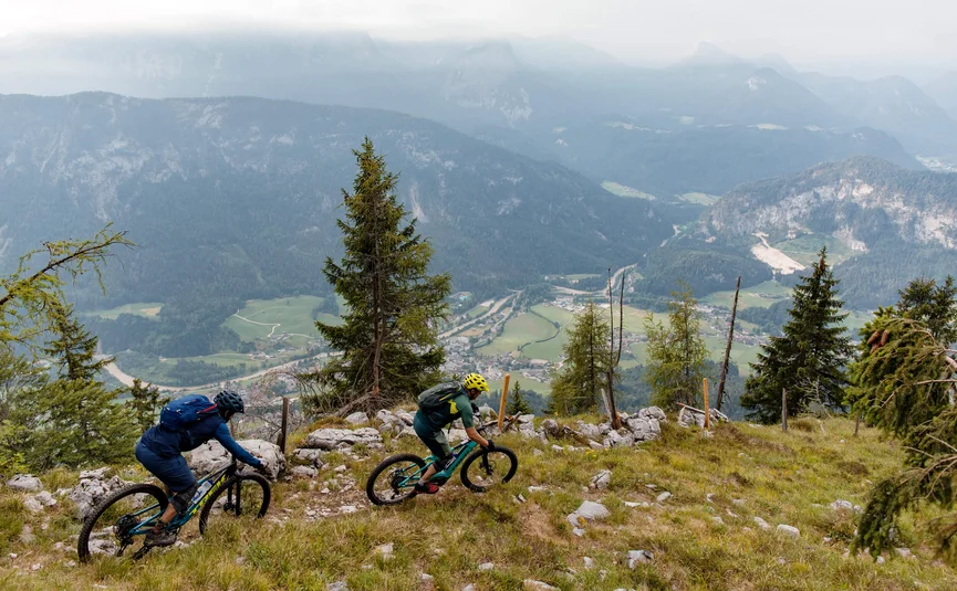 Two mountain bikers riding on a mountain trail overlooking a valley