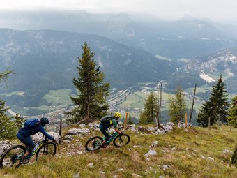 Zwei Mountainbiker fahren auf einem Bergpfad mit Talblick