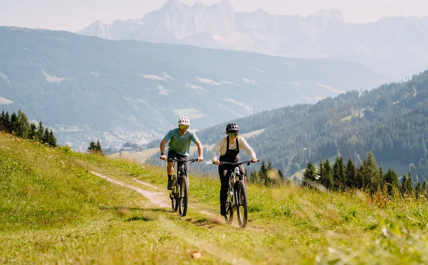 Twee mensen mountainbiken op een groen bergpad