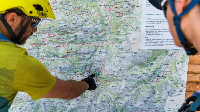 Zwei Radfahrer mit Helm und Handschuhen schauen auf eine Wanderkarte.