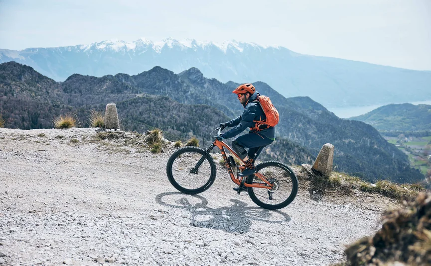 Mountainbiker fährt auf einem felsigen Bergpfad mit schneebedeckten Bergen im Hintergrund