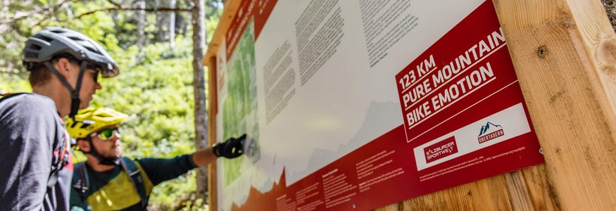 Zwei Mountainbiker schauen sich eine Infotafel mit Streckenplan an