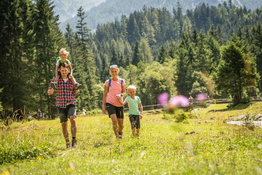 Familie wandert mit Kindern auf einer grünen Wiese in den Bergen