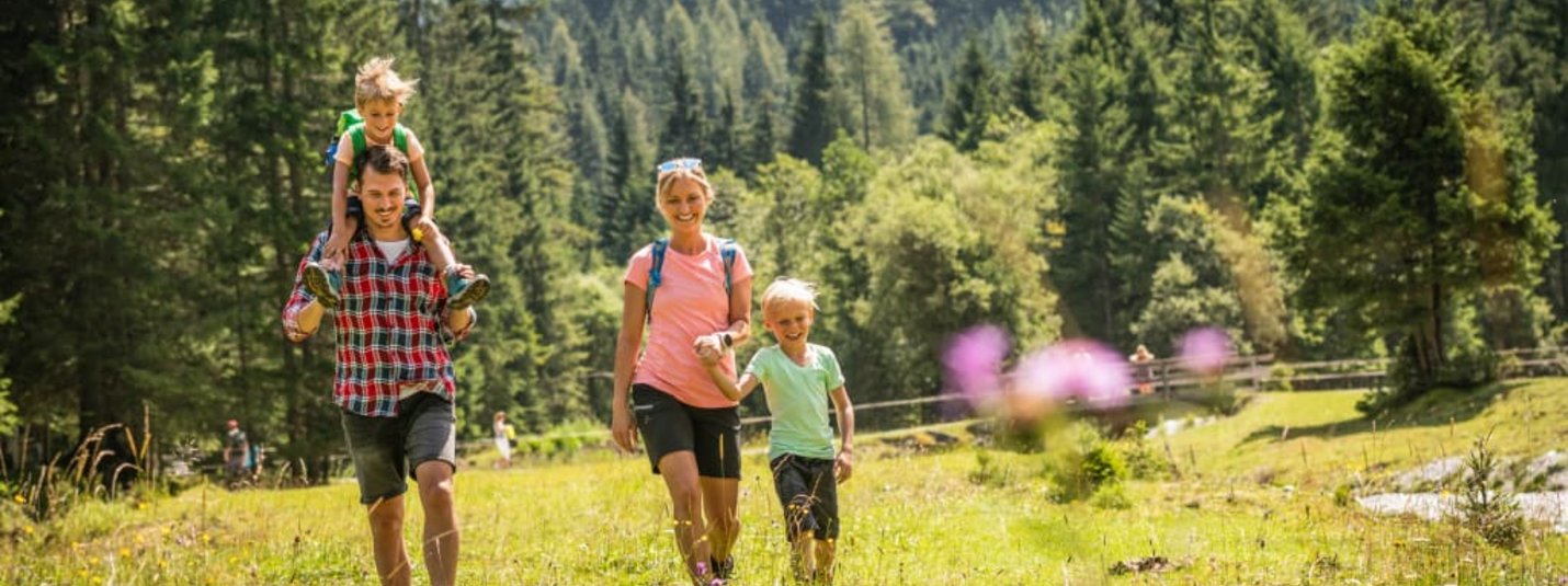 Familie wandert mit Kindern auf einer grünen Wiese in den Bergen