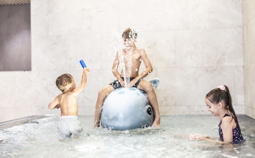 Three children playing in water, one sitting on a dolphin water spray toy.