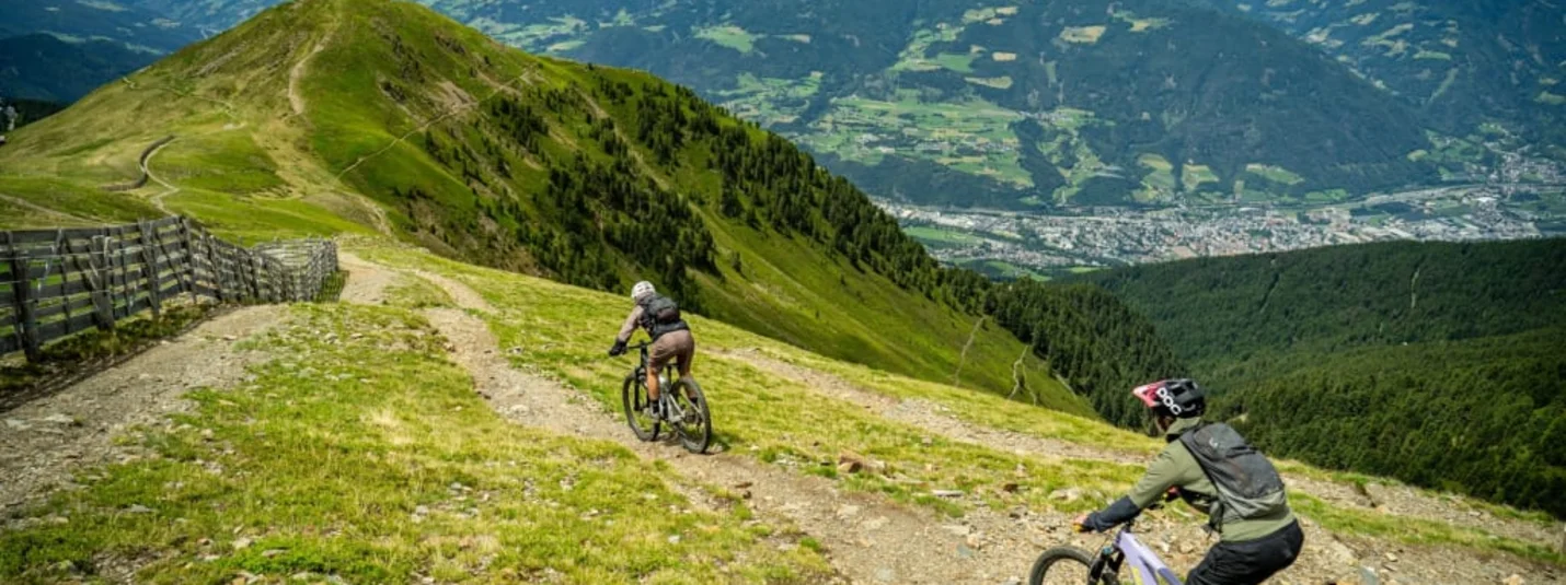Two mountain bikers on a trail with valley and mountain scenery in background