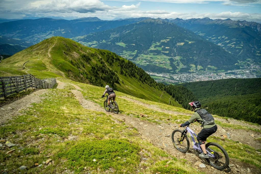 Two mountain bikers on a trail with valley and mountain scenery in background