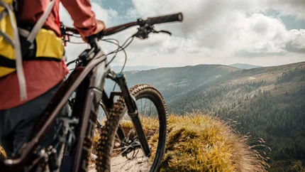 Mountainbiker kijkt uit over beboste heuvels onder een bewolkte hemel