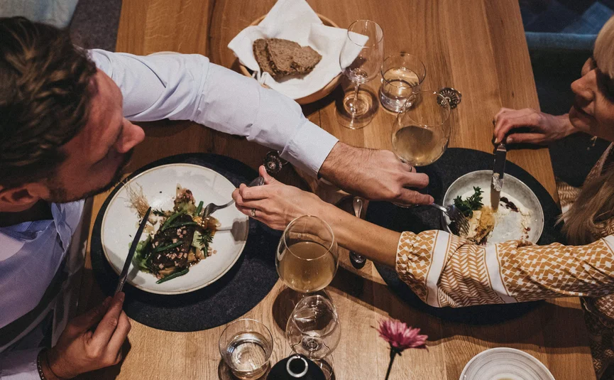 Pärchen teilt Essen und Wein bei gemütlichem Abendessen am Holztisch