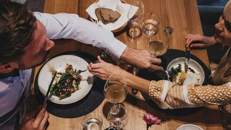 Was steckt hinter dem Umweltengagement von Bikehotels? © Biohotel Rupertus Pärchen teilt Essen und Wein bei gemütlichem Abendessen am Holztisch