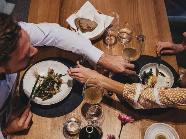 Was steckt hinter dem Umweltengagement von Bikehotels? © Biohotel Rupertus Pärchen teilt Essen und Wein bei gemütlichem Abendessen am Holztisch