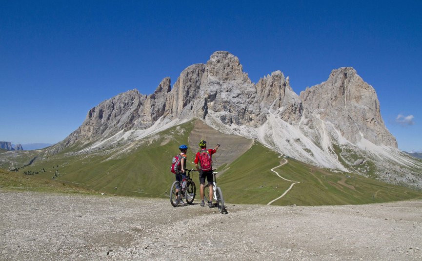 Hotel Pider ***S © Hotel Pider Zwei Radfahrer betrachten die Dolomiten unter klarem blauem Himmel